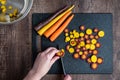 WomanÃ¢â¬â¢s hands cutting rainbow carrots on a black cutting board, stainless-steel bowl, wood table Royalty Free Stock Photo